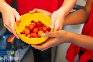 hands holding a yellow bowl of tomatoes and berries