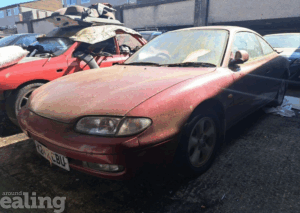 Dirty red car with another dirty, damaged car in the background