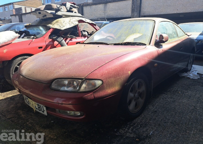 Dirty red car with another dirty, damaged car in the background