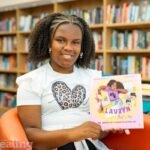 author Lauryn sitting in Ealing Library holding her book