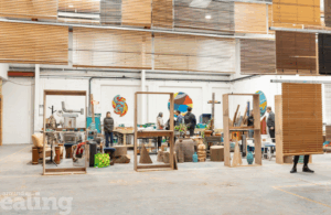 A large open space with tables and many wooden creations. Some people walking around. Artwork on the walls