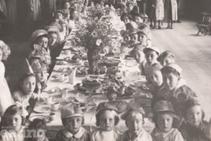 sepia image of children and women enjoying a big tea party to celebrate VJ Day in Southall