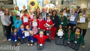 The winners of the Ealing Biodiversity Awards for Gardens and Green Spaces. A group of smiling winners of the awards including children and adults holding certificates and one of them is holding a trophy.