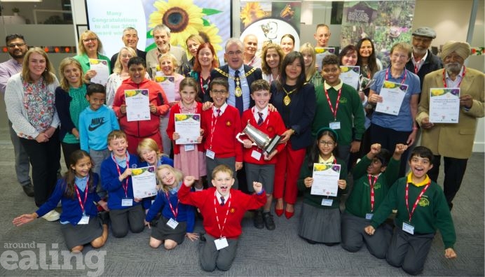 The winners of the Ealing Biodiversity Awards for Gardens and Green Spaces. A group of smiling winners of the awards including children and adults holding certificates and one of them is holding a trophy.