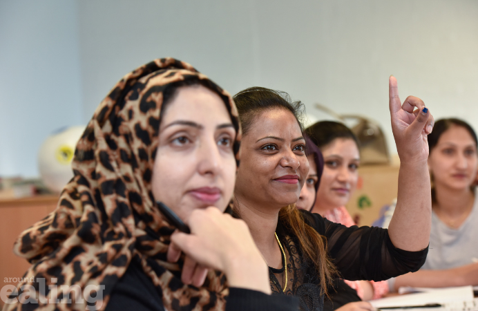 4 women sitting next to each other in what looks like a classroom. One woman has her hand raised