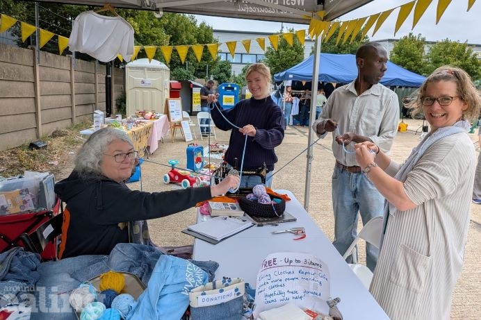 Ealing Repair Cafe stall at ReActon event. Event-goers stood behind table holding yarn, with stall-holder holding the other end of the yarn.