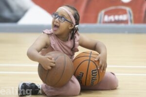 Girl with SEND smiling in sports hall holding 2 basketballs