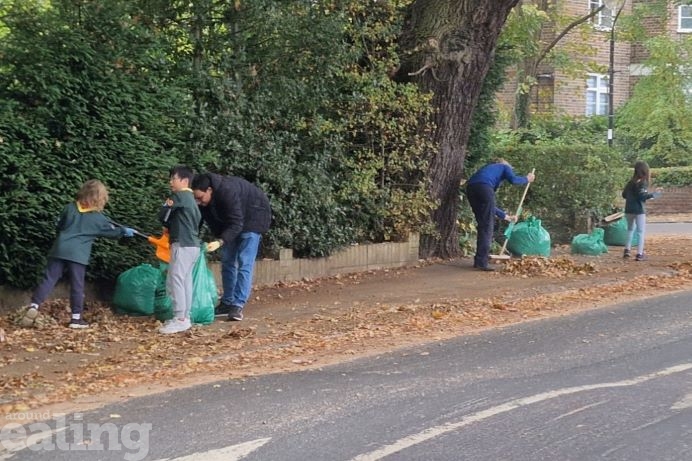 Photo of Scout Cubs and leader sweeping leaves into green sacks on the pavement