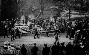 Funeral cortege from 1906 with soldiers in uniform walking alongside a coffin draped in the Union Flag and pulled on a cart by horses