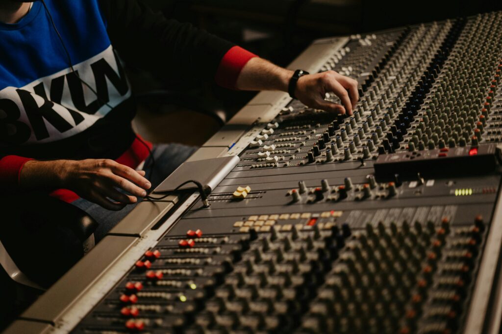 Close-up of an audio technician adjusting controls on a large professional mixing console with multiple knobs, sliders, and switches.