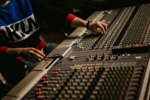 Close-up of an audio technician adjusting controls on a large professional mixing console with multiple knobs, sliders, and switches.