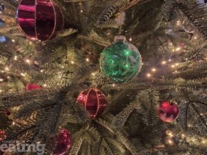 A close up photo of a Christmas tree. There are red and green baubles on the tree.