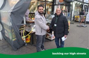 Shop owner shaking hands with Ealing Council's waste commercial sales officer in front of high street shops