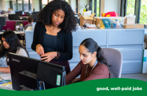A person on work experience talking to a staff member. Sat at desk with monitor