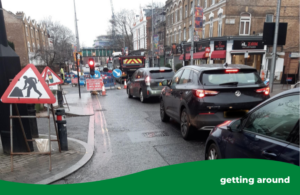 Cars queuing in traffic behind a roadworks sign and a red light signal