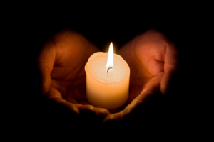 A picture of two hands holding a candle surrounded by darkness