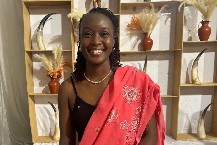 A woman smiling at the camera. A shelf and decorations behind her