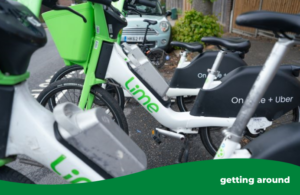 Three green and white electric Lime bikes are standing in a row in an-e-cycle parking bay in the road. At the bottom right there is a green frame with the words getting around.
