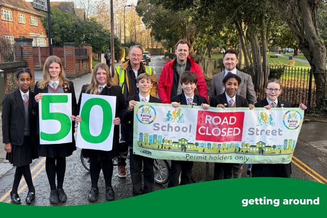 Headteacher, councillors, and students stood at the end of a street, children holding a banner and '50' sign