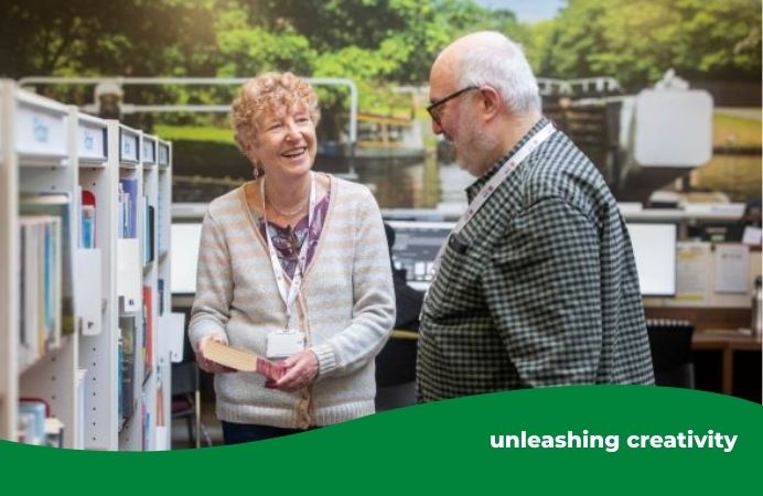 man and woman library volunteers smiling in conversations at the bookshelves