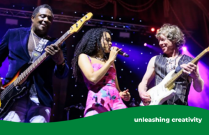 Three members of the band Brand New Heavies on stage at Ealing jazz festival. From left to right there is a man with a guitar smiling, a woman singing into a microphone and a man smiling at her with a guitar.