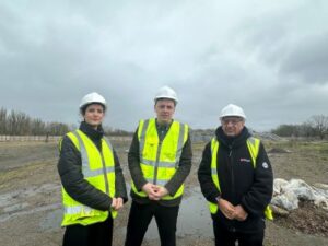 Three councillors with flourescent yellow waistcoats and hard hats standing outside.