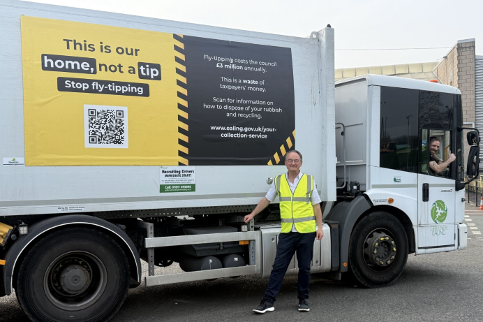 Councillor Paul Driscoll stood in front of a fly-tip branded refuse vehicle, wearing a high-visibility jacket. A driver is leaning out of the window with his thumb up