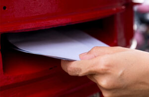 A hand pushing envelopes into a Post Office post box on a street