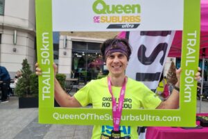 man in running gear holding up a Queen of the Suburbs picture frame