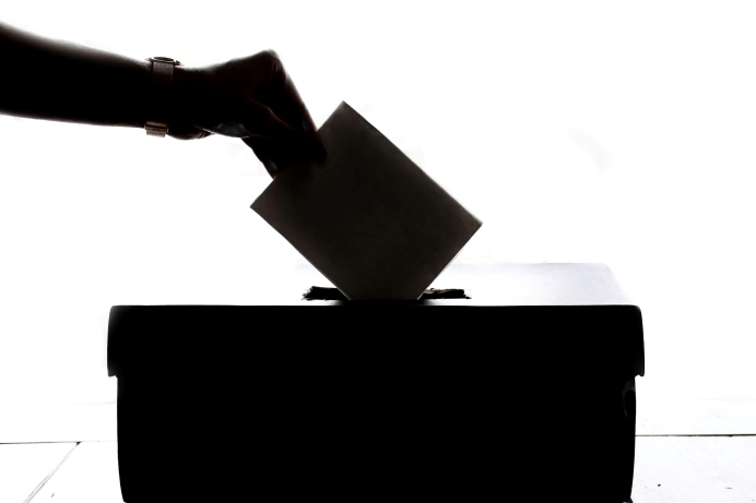 Silhouette of a hand placing a voting slip into a ballot box