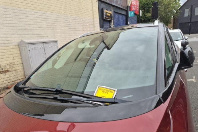 Front of a red car with a yellow penalty charge notice tucked in the windscreen wiper