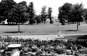 Flower beds, a path and trees, with a house in the far distance