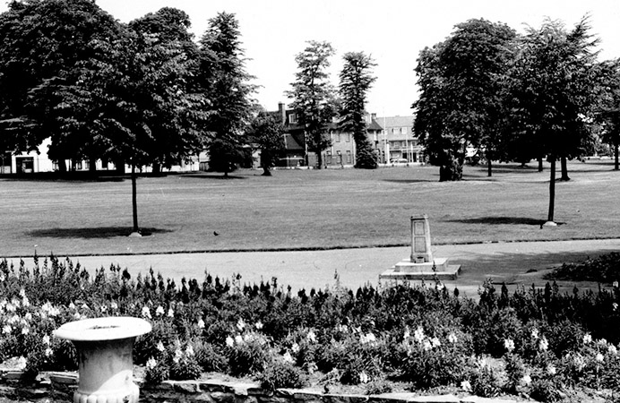 Flower beds, a path and trees, with a house in the far distance