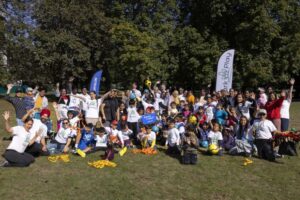 Large group of children and adults gathered in a park for a ParkPlay community sports session, raising hands and holding equipment. “Ready to play?” sign visible against a backdrop of trees on a sunny day