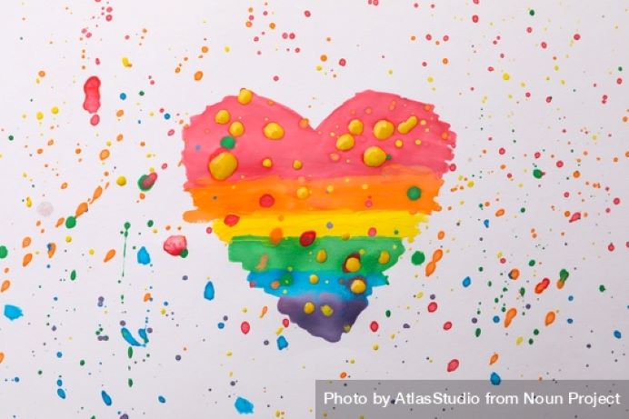A heart painted with rainbow colours on a white background with rainbow paint flicks all over it and the white background.