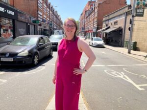 Samantha Steggles is wearing a pink sleeveless jumpsuit standing in the middle of Bond Street in Ealing with cars on either side of her.