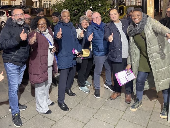 A group of people standing in front of a Christmas tree smiling and giving thumbs up at the camera.