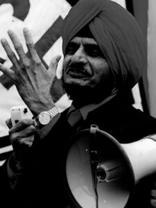 A Sikh man wearing a turban speaking into a loudspeaker