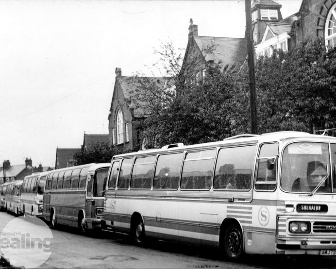 A black and white image of two coaches parked outside a school in Southall.