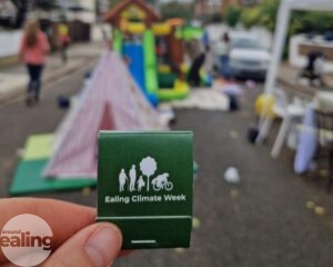 A close up picture of a small pack of matches with the Ealing Climate Week logo on. In the background is a child's play tent and other games for a play street.
