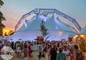 A large white marquee structure with lots of people standing and chatting in front of it.