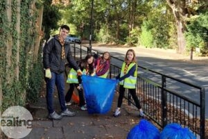 Scout leader and 3 children holding a blue bag with leaves on a pavement