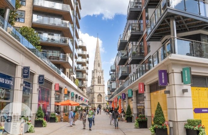 A high street with people walking down it and a church in the distance